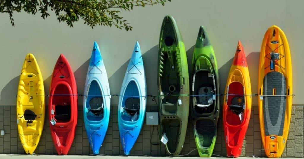 Eight of the best kayaks for camping lined up on a wall outside.