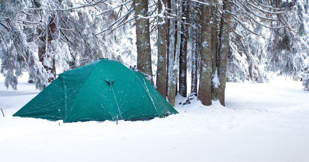 green tent set up in a snowy landscape for the article: how to heat a tent without electricity?