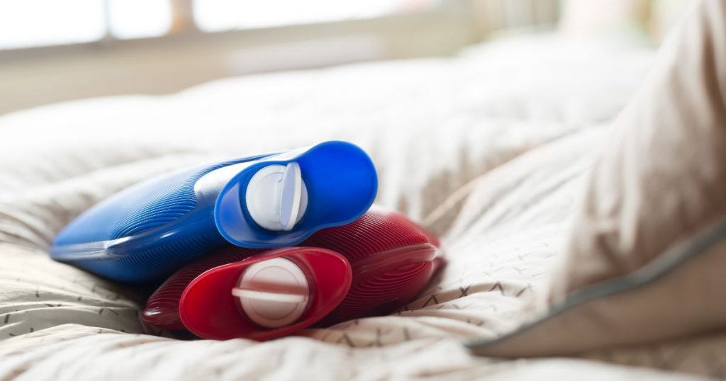 image of two hot water bottles stacked on a bed (blue and red) for the article: how to heat a tent without electricity.