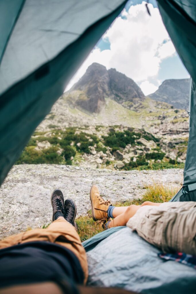 summer camping near a mountain. 2 people in a tent.